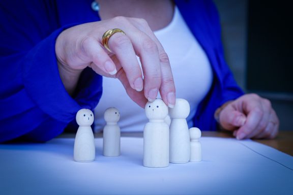 Aufstellung Eine Hand platziert eine Figur auf einer Gruppe von Holzfiguren auf einem Tisch.